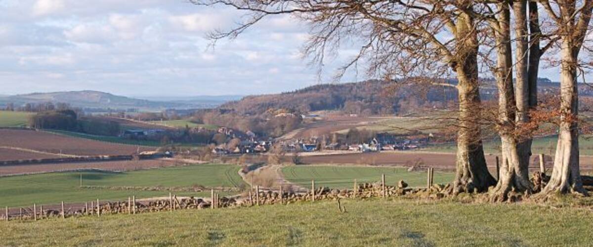 A rural landscape with rolling hills, a winding road, and a small village in the distance.