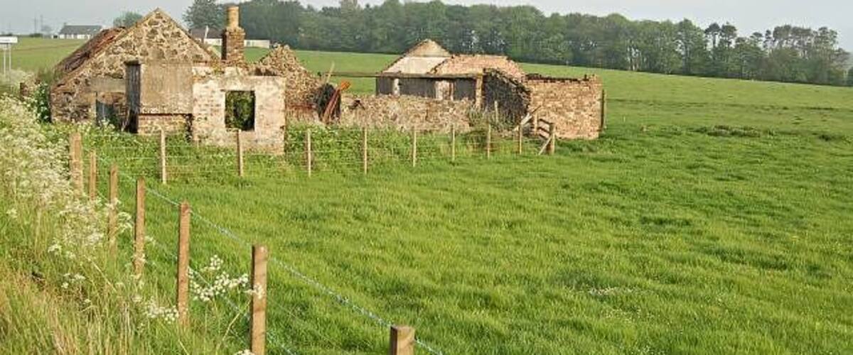 A rural landscape with a fenced field, a dilapidated stone building, and a smaller structure in the background.