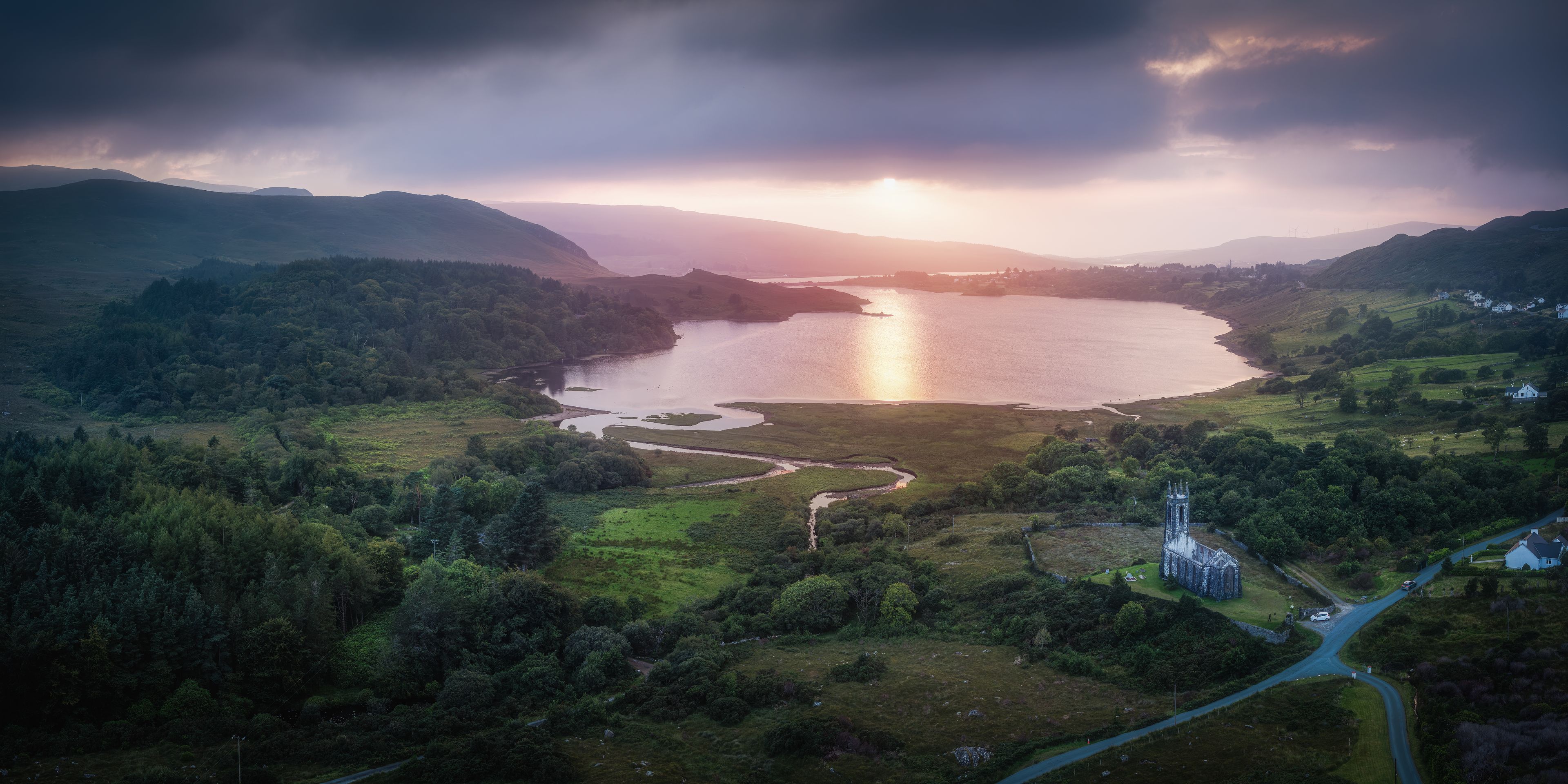 A lake surrounded by hills, a church, and a winding road.