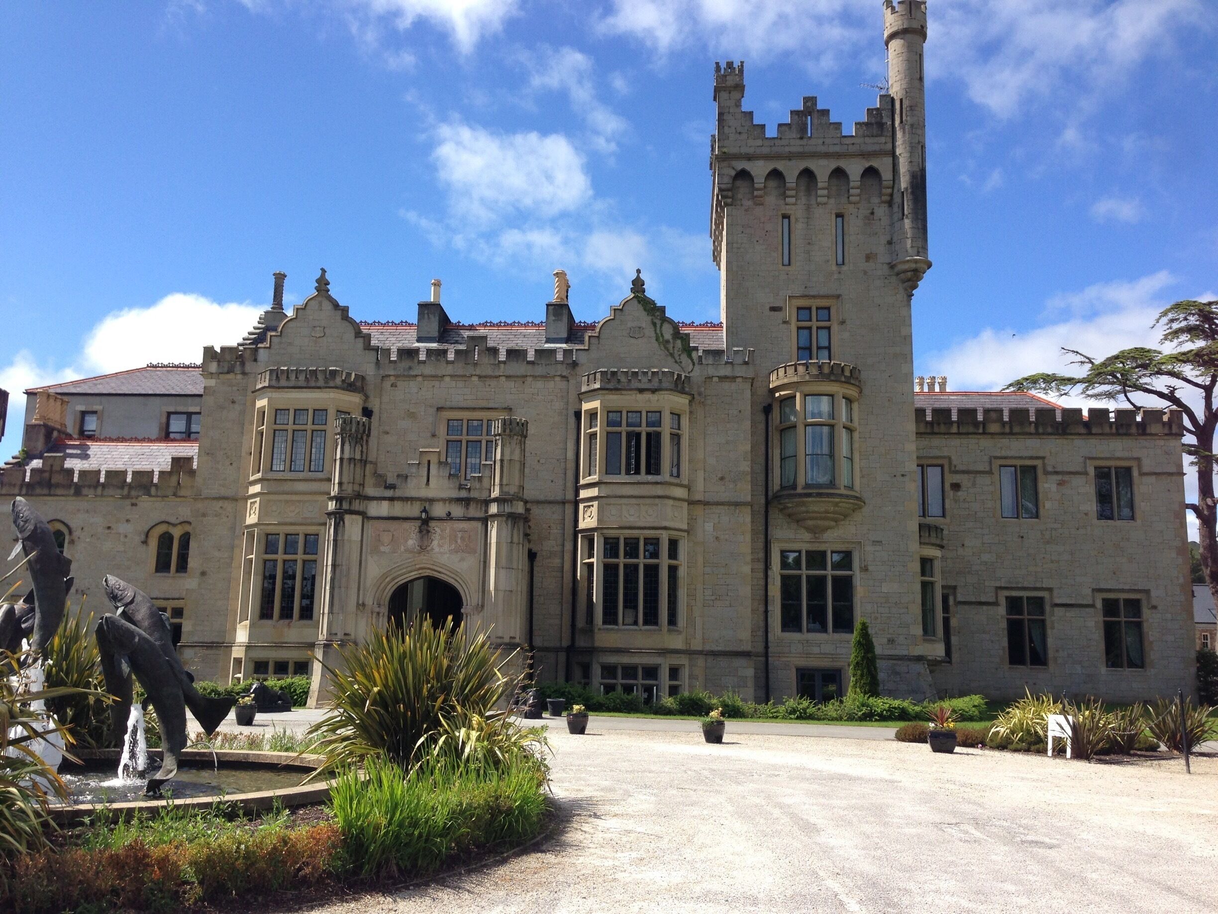 A historic stone building with a tower, statues, and a fountain.