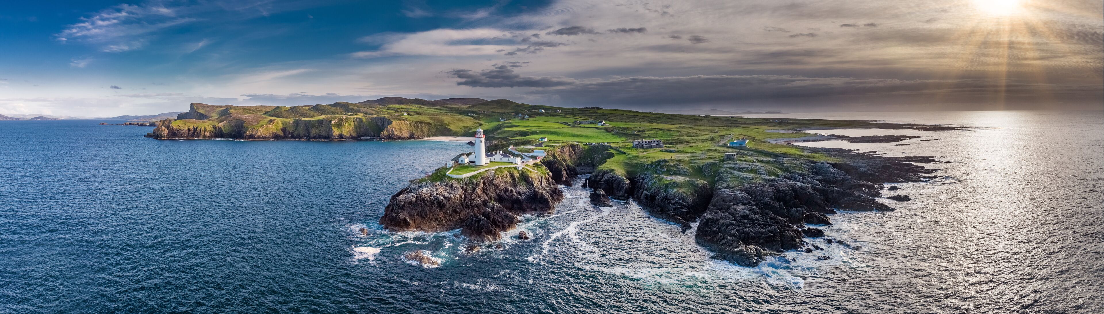 A coastal landscape with a lighthouse, grassy cliffs, and a calm sea.