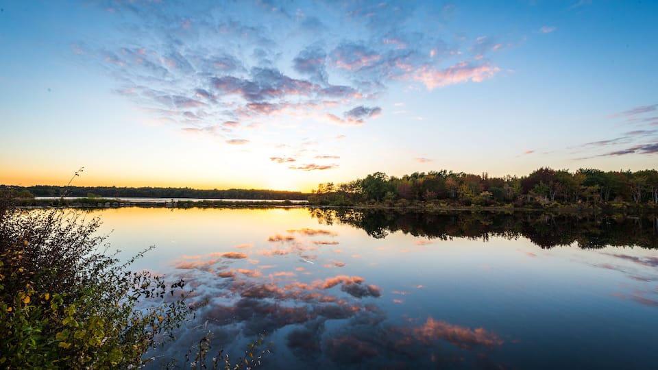 A calm lake at sunset with a clear sky and trees in the background.