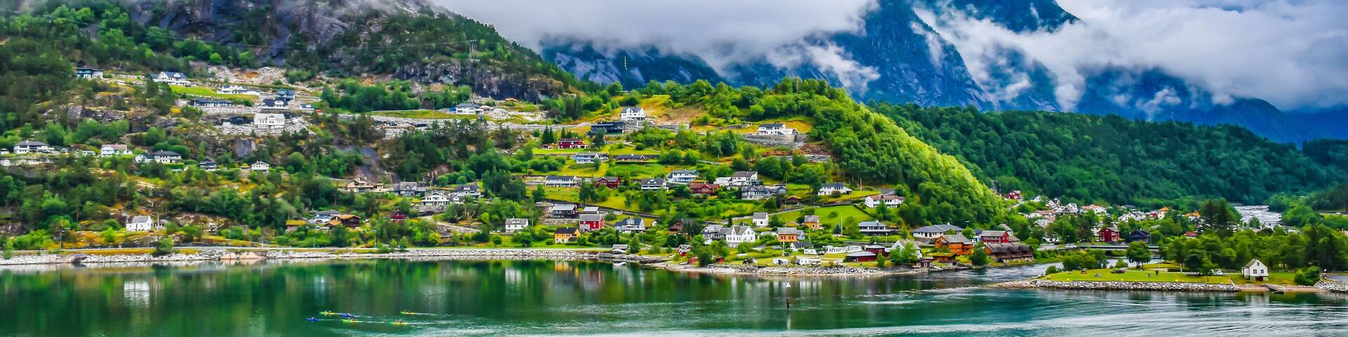 A mountainous village with houses nestled among lush greenery and a lake in the foreground.