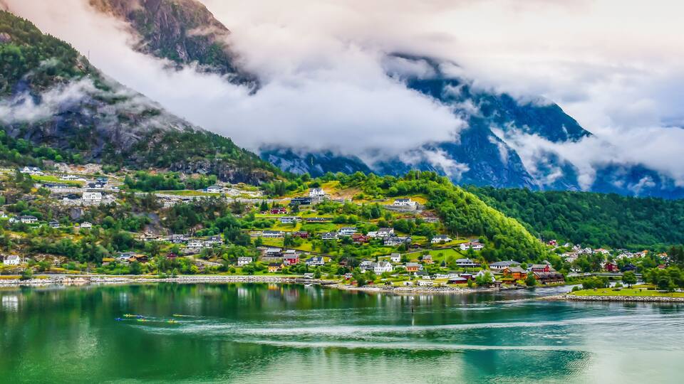 A mountainous village with houses nestled among lush greenery and a lake in the foreground.