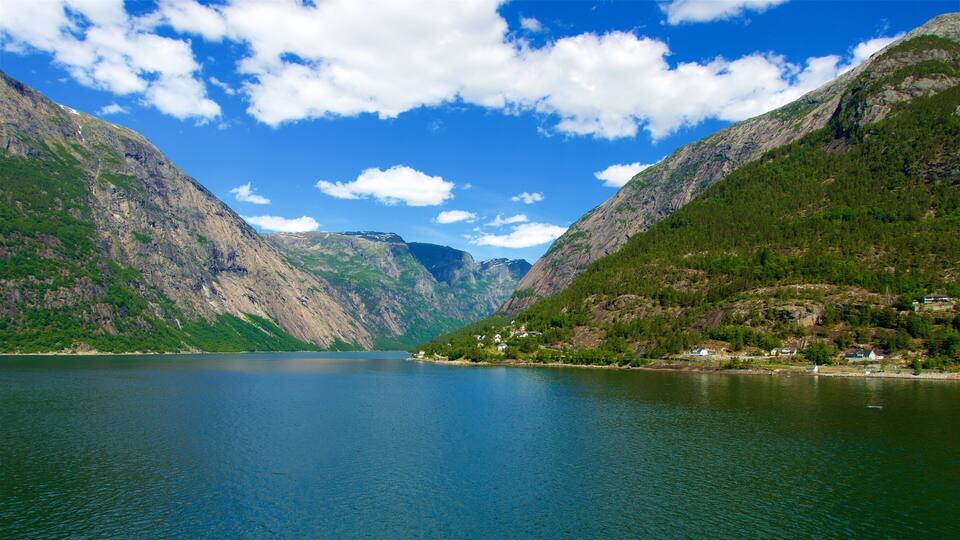 A calm lake surrounded by steep, forested mountains under a clear sky.