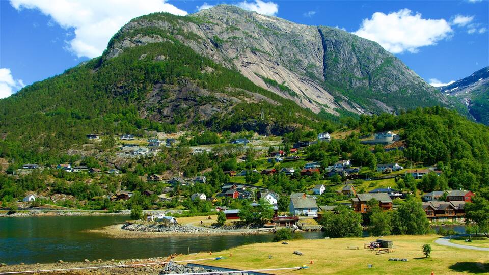 A mountainous landscape with a lake, houses, and a prominent rocky peak.