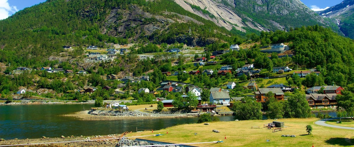 A mountainous landscape with a lake, houses, and a prominent rocky peak.