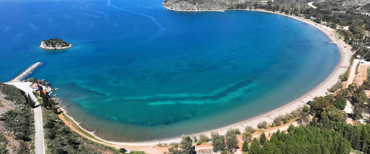 A coastal landscape with a clear blue sea, a sandy beach, and a small island.