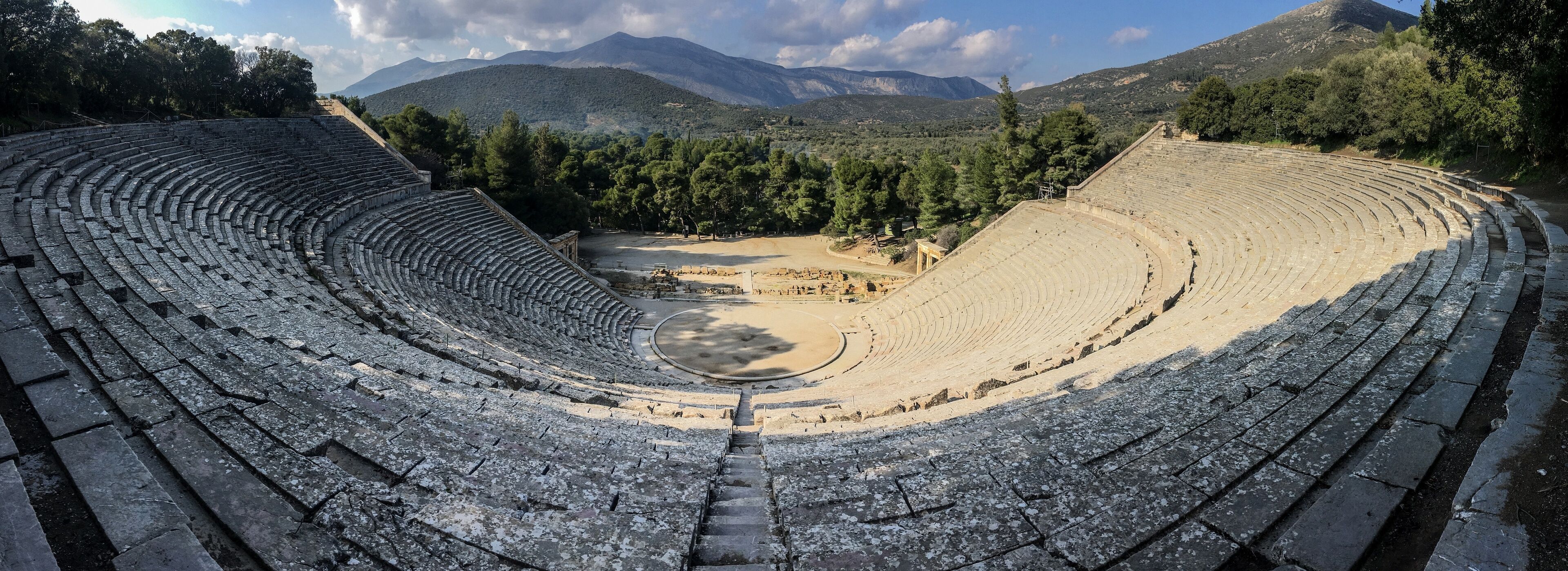 An ancient amphitheater surrounded by mountains and trees.