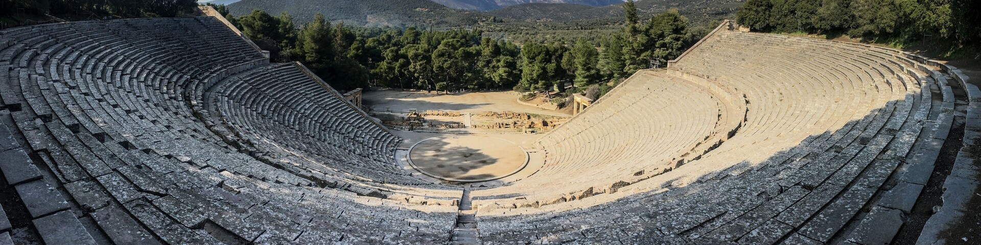 An ancient amphitheater surrounded by mountains and trees.