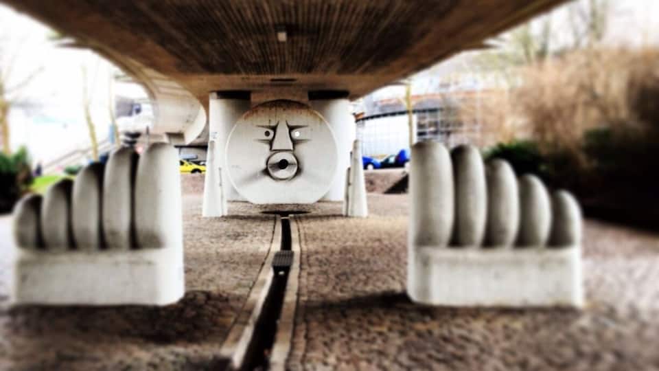 A railway track under a bridge with concrete supports and a circular metal structure.