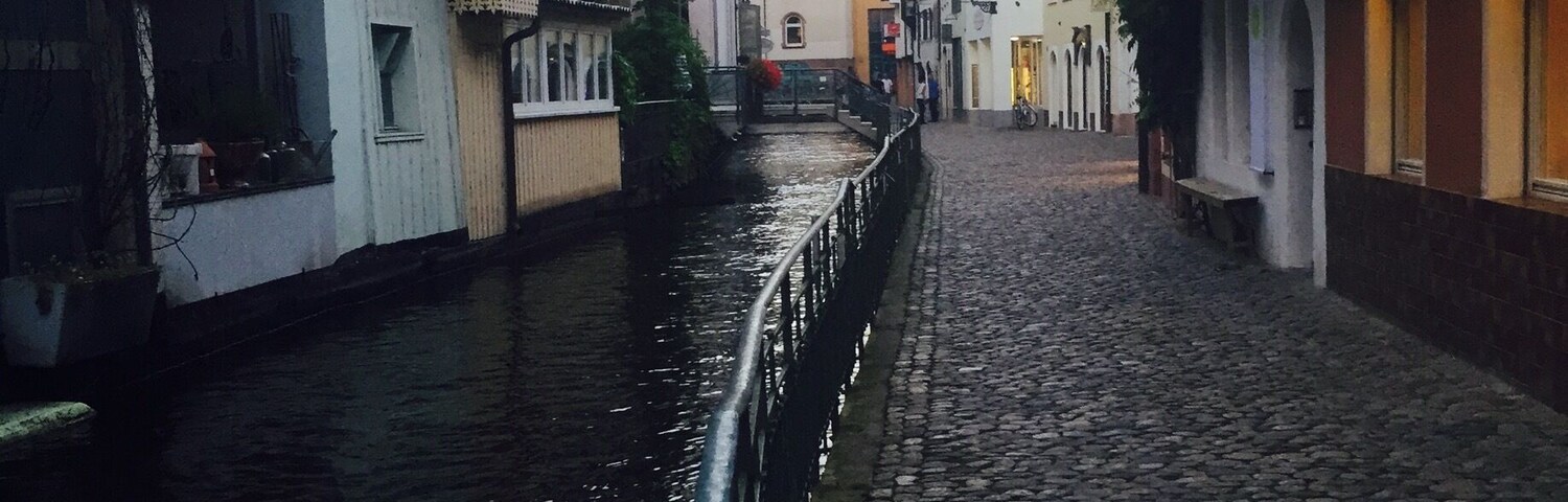 Una estrecha calle adoquinada bordeada por edificios con balcones y un canal.