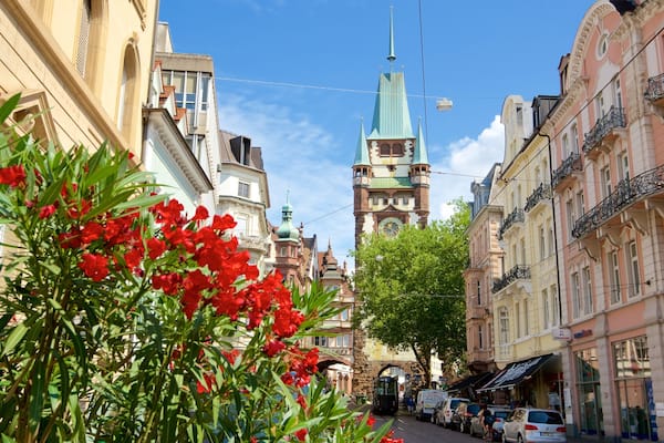Eine Straße mit historischen Gebäuden, einem Kirchturm und roten Blumen im Vordergrund.