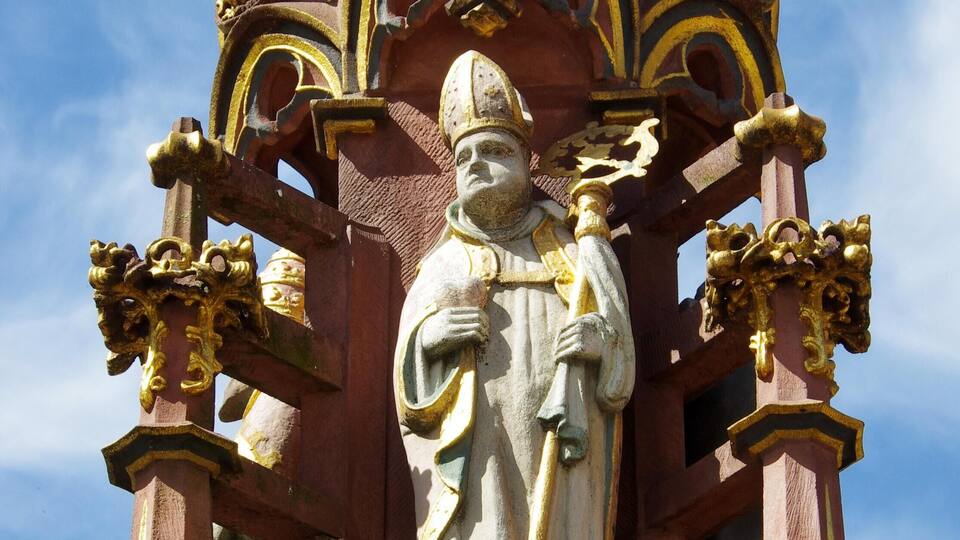 A detailed statue of a figure holding a staff, surrounded by ornate gold and red architectural elements.