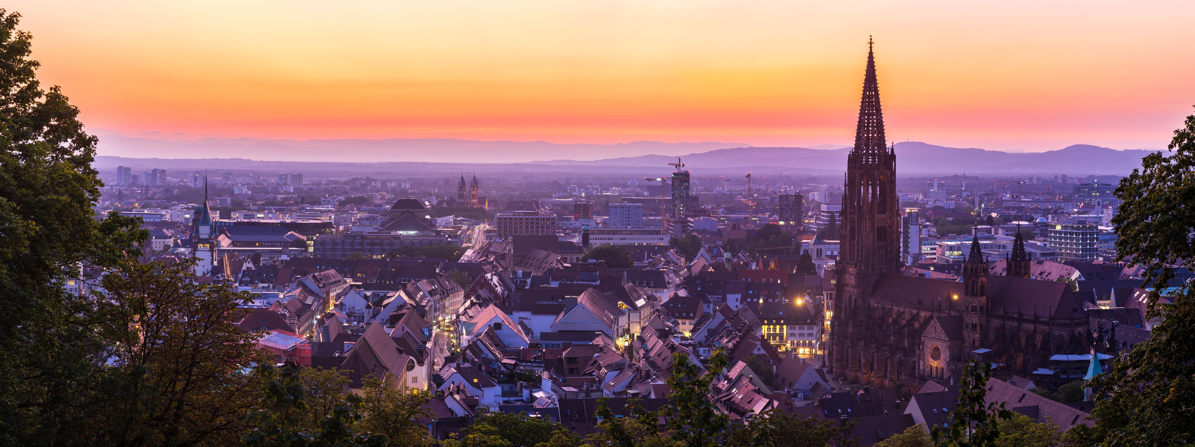 A cityscape at sunset with a prominent cathedral and surrounding buildings.