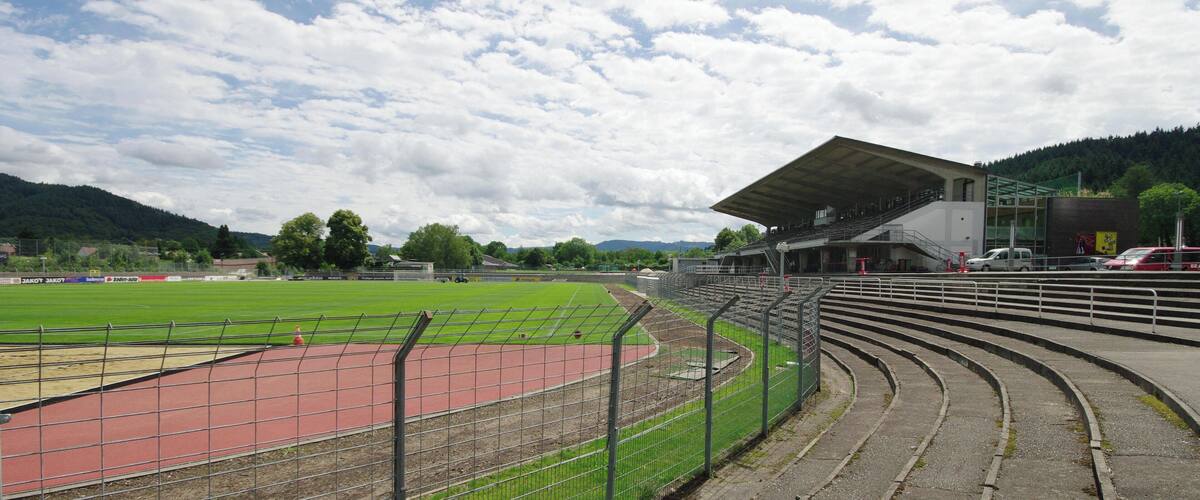 A sports stadium with a running track, bleachers, and a covered seating area.