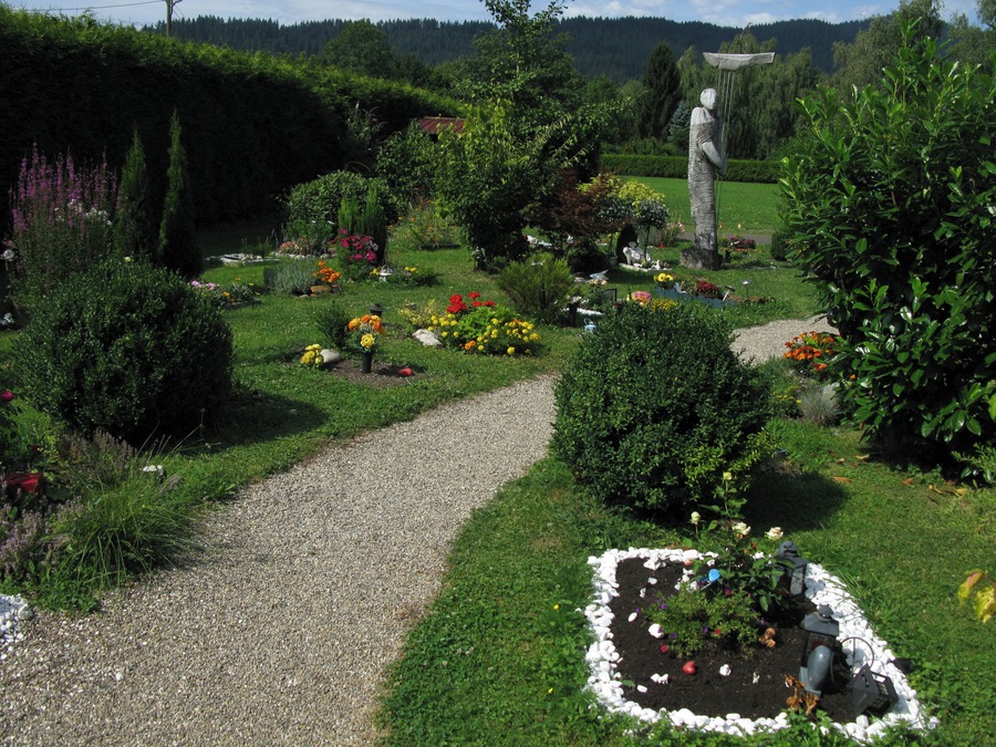 Um jardim com um caminho de cascalho, diversas flores e uma estátua.