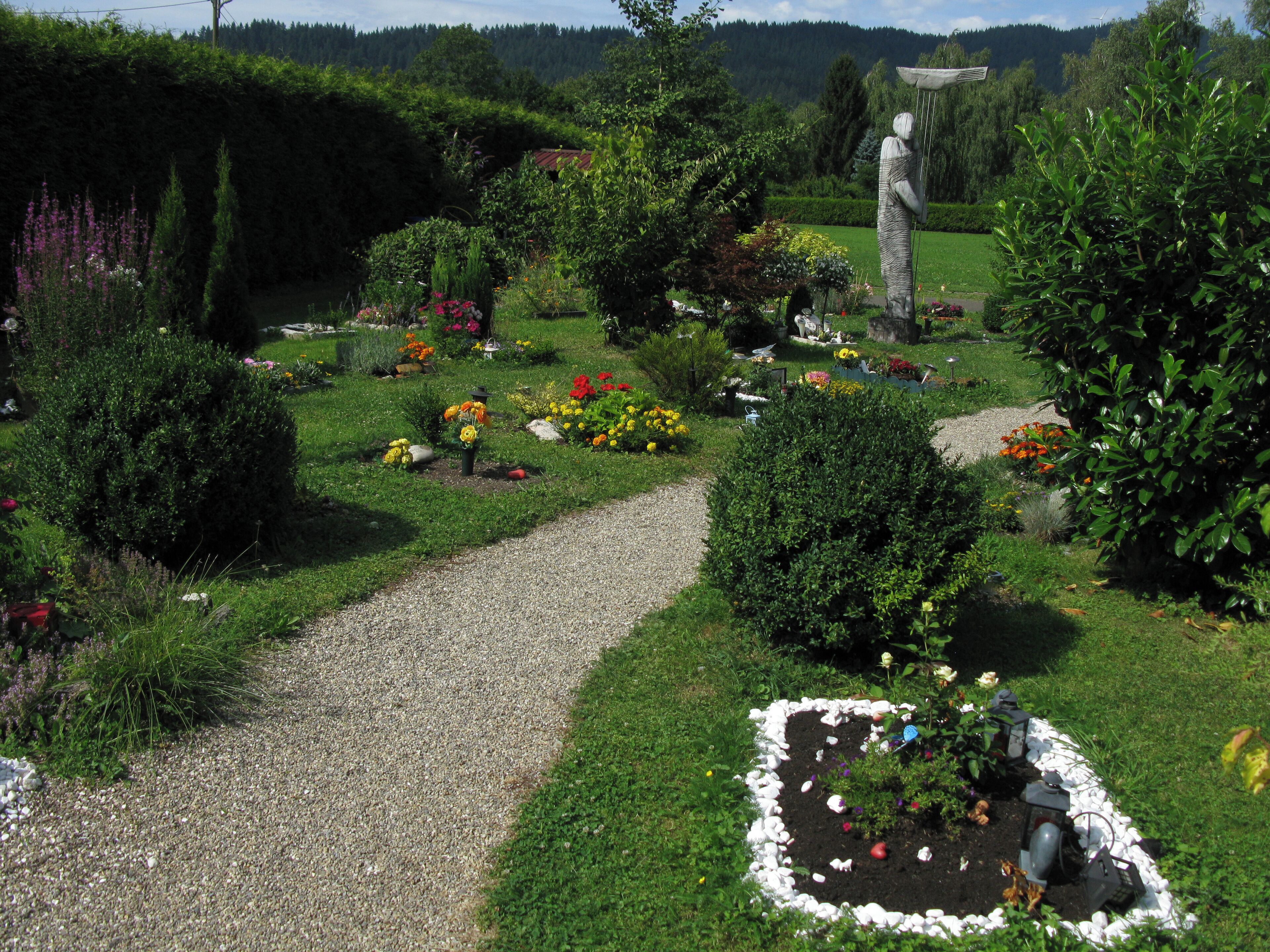 A garden with a gravel path, various flowers, and a statue.