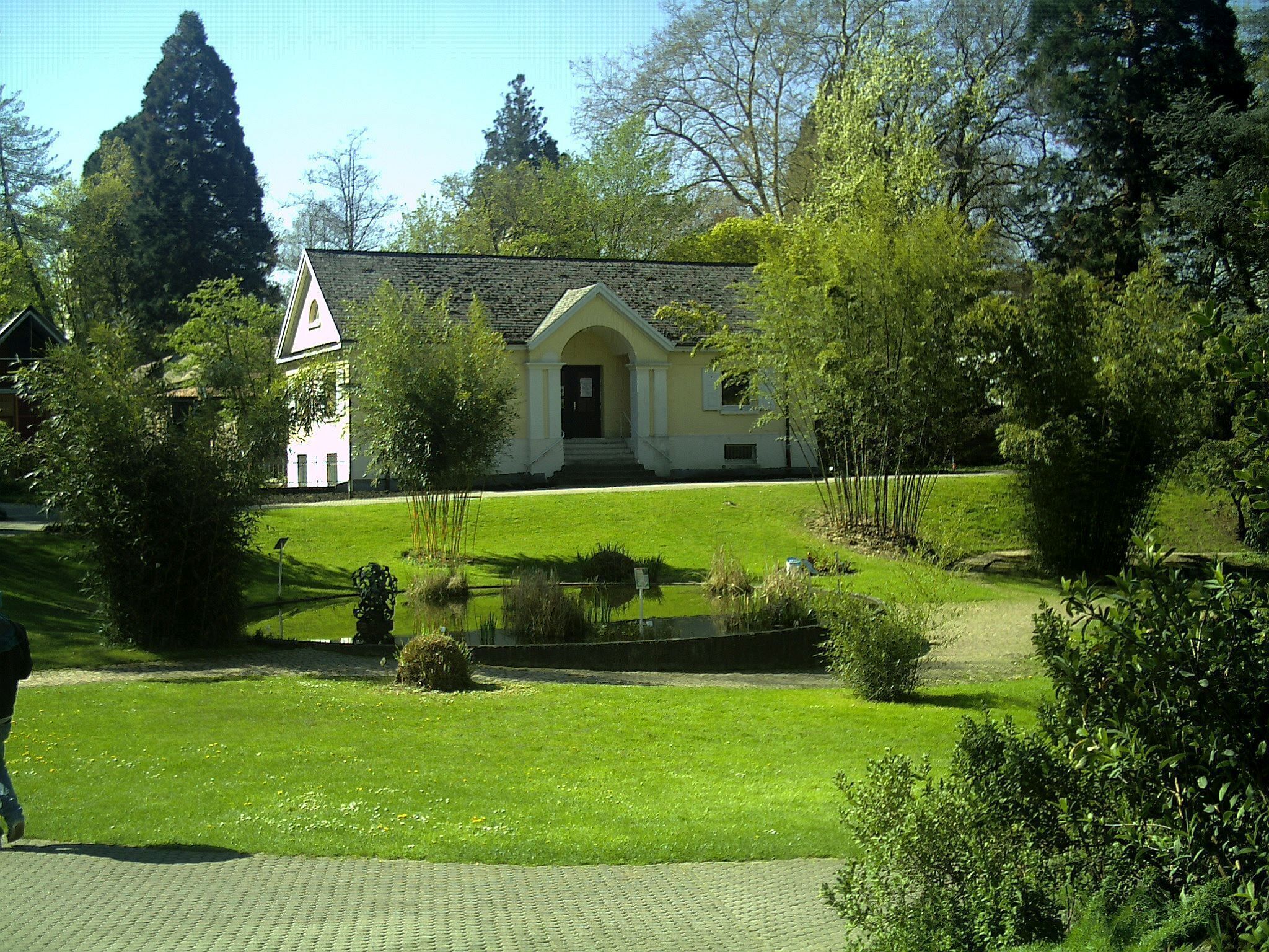 A building with a white facade and a red door, surrounded by a well-maintained lawn and a small pond.