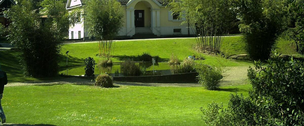 A building with a white facade and a red door, surrounded by a well-maintained lawn and a small pond.