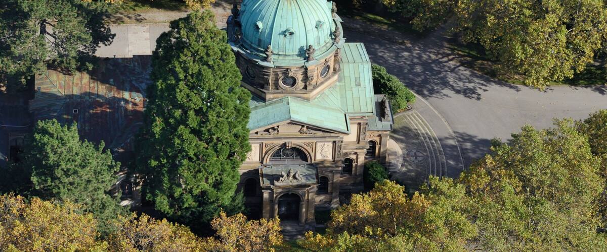 An aerial view of a historic building with a large dome, surrounded by dense trees.