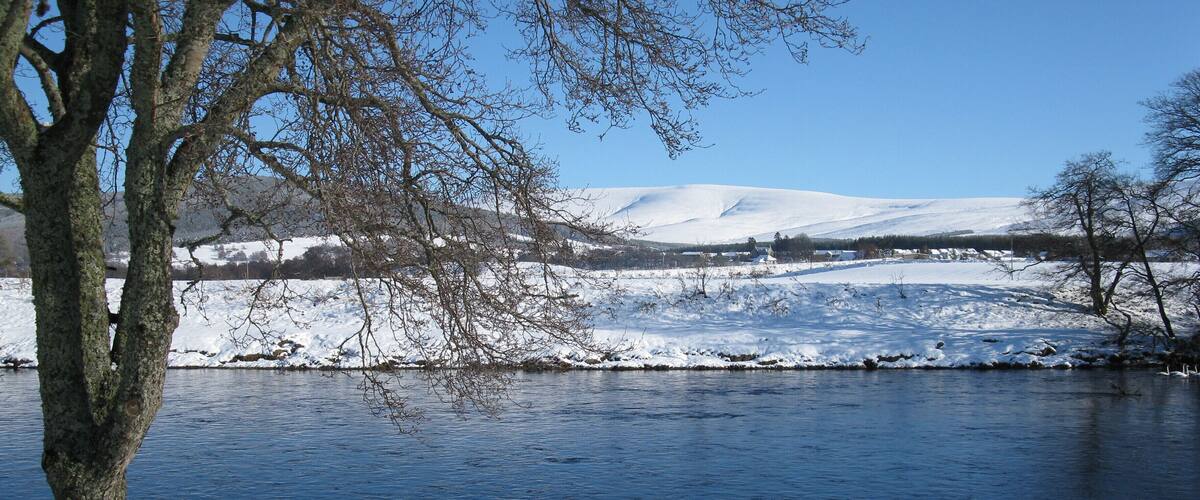 A snow-covered landscape with a river, trees, and distant hills.
