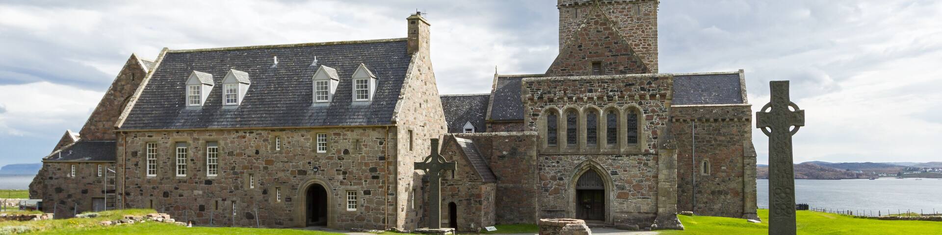 A historic stone building with a tower and a large cross in the foreground.