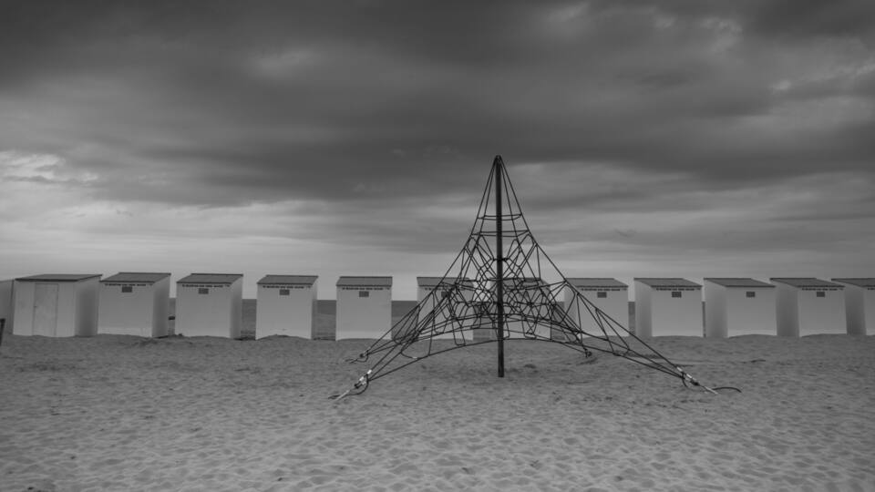 A beach with a metal sculpture in the center and beach huts in the background.