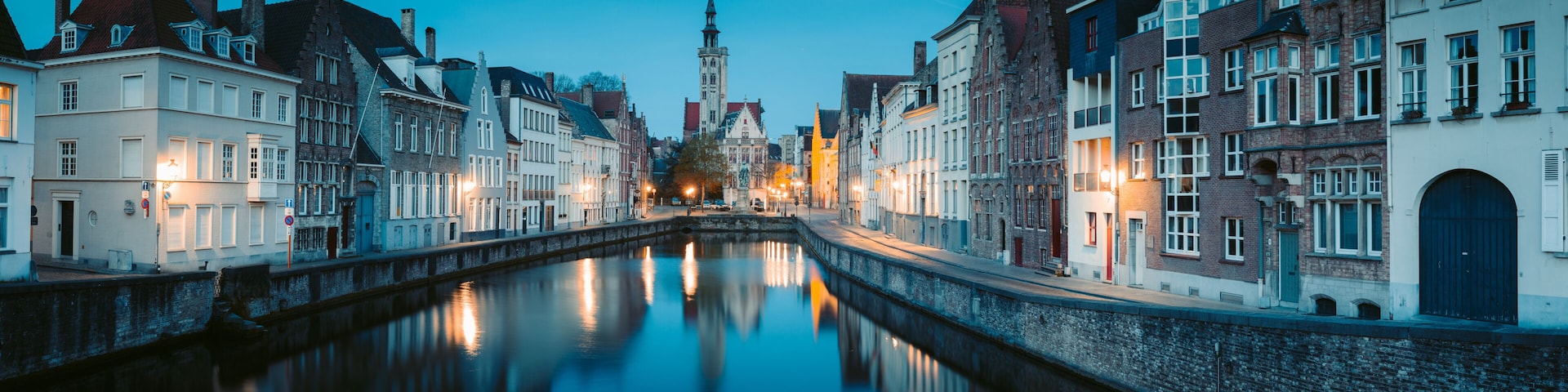 A canal with buildings on either side, a tower in the distance, and a clear sky.