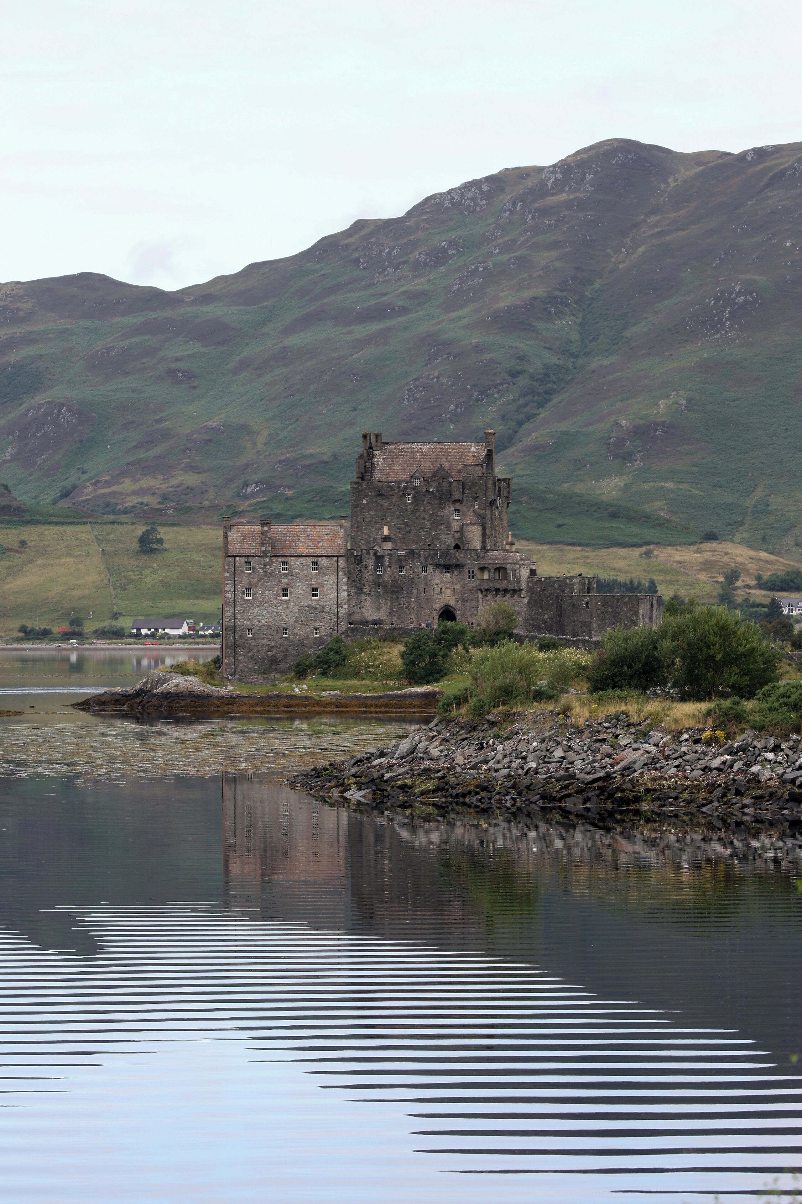 A historic castle by a calm lake with surrounding green hills.