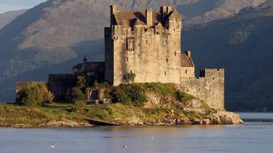 A historic castle on a lakeside with mountains in the background.