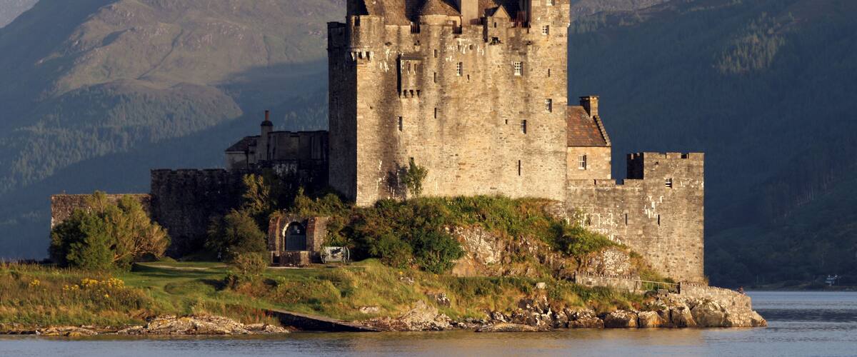A historic castle on a lakeside with mountains in the background.