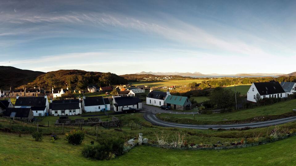 A coastal village with white houses, a winding road, and rolling hills in the background.