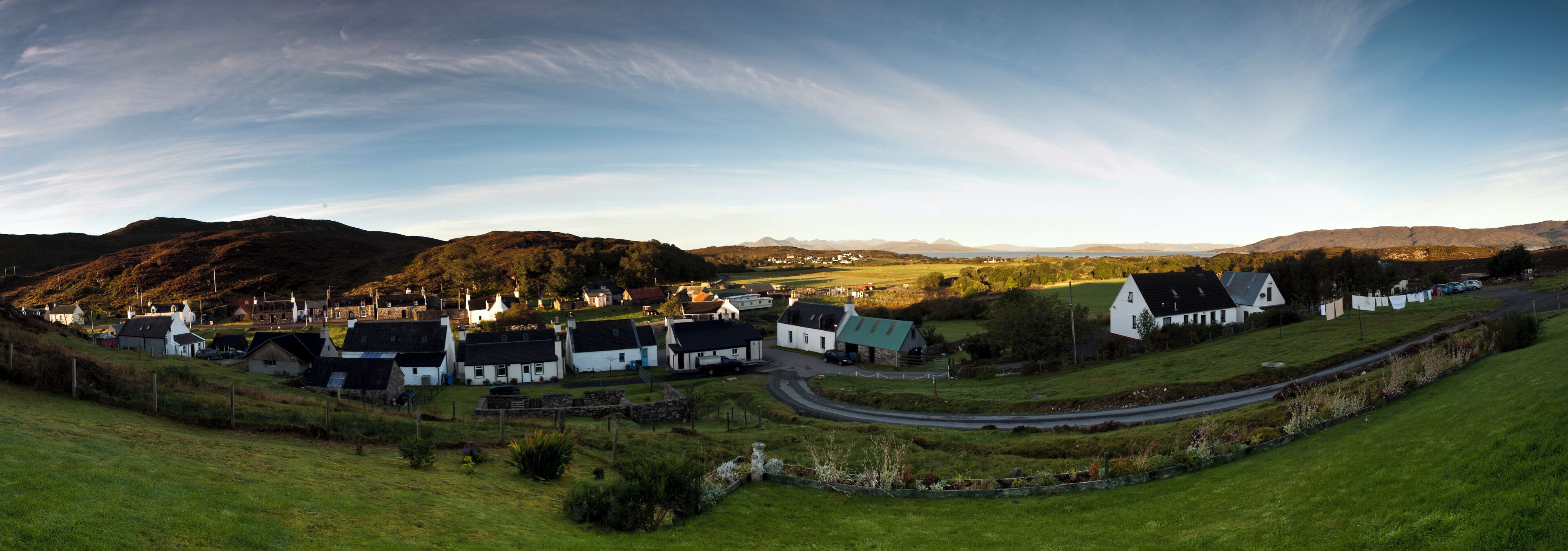 A coastal village with white houses, a winding road, and rolling hills in the background.