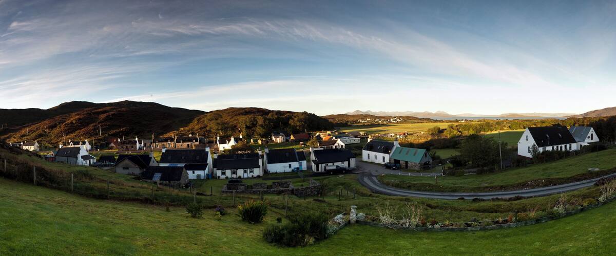 A coastal village with white houses, a winding road, and rolling hills in the background.