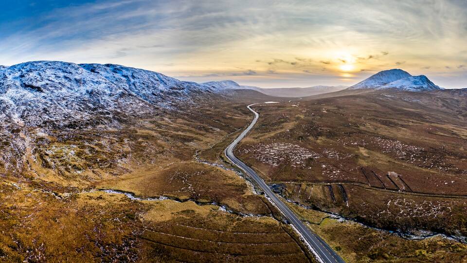 A snow-covered mountain range with a winding road through a valley.