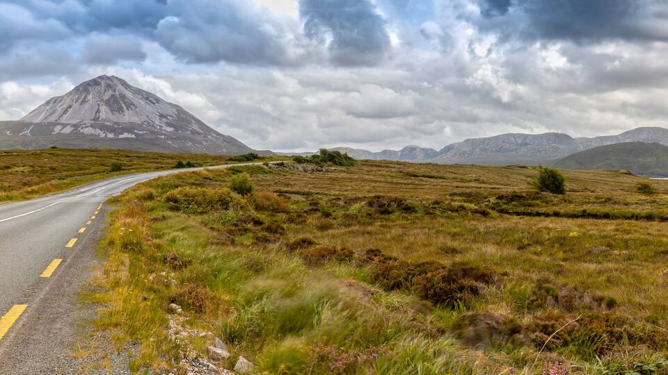 A winding road through a grassy landscape with a mountain in the background.