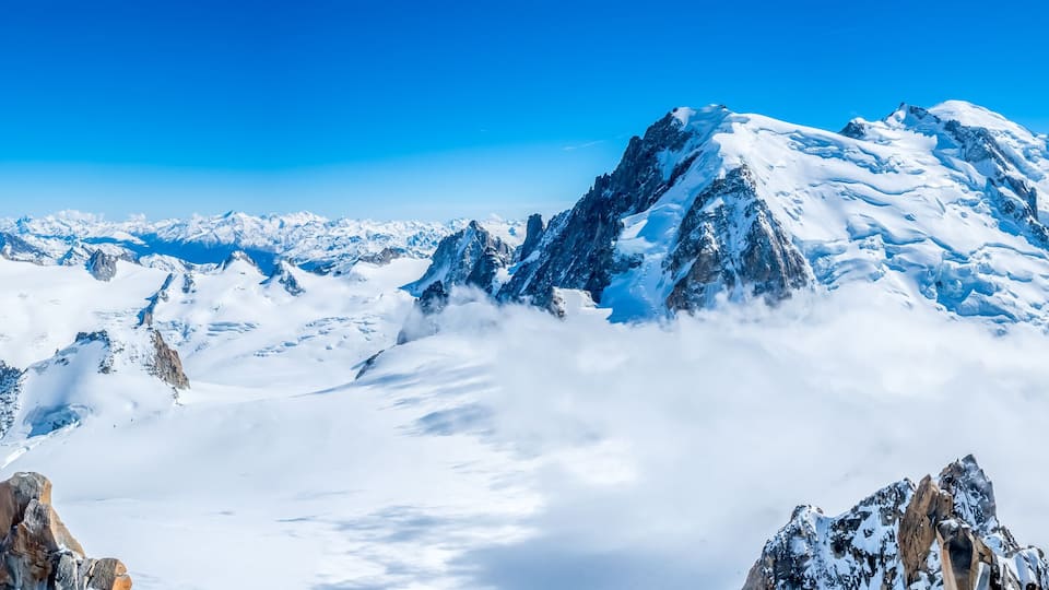Snow-covered mountain peaks, rocky outcrops, and a clear blue sky.
