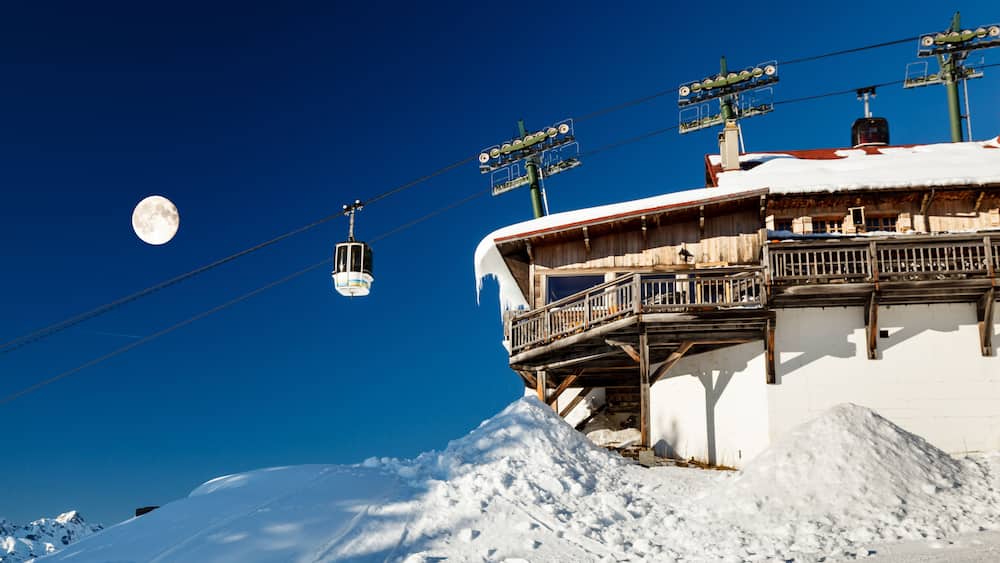 Ein schneebedeckter Berg mit einer Seilbahn und einem Mond am Himmel.