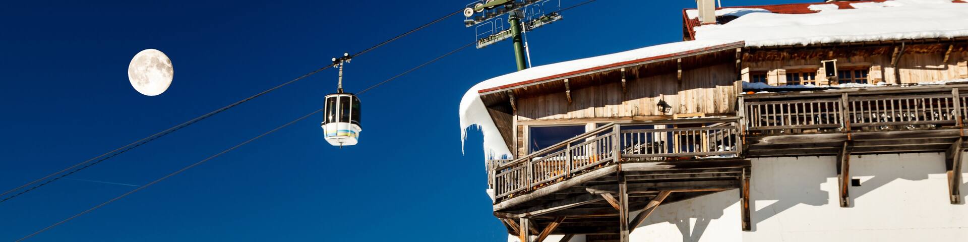 A snow-covered mountain with a ski lift and a moon in the sky.