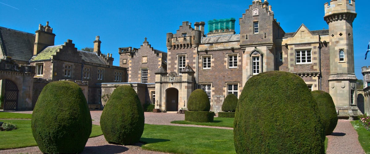 A historic building with a tower, surrounded by well-manicured hedges and a gravel path.