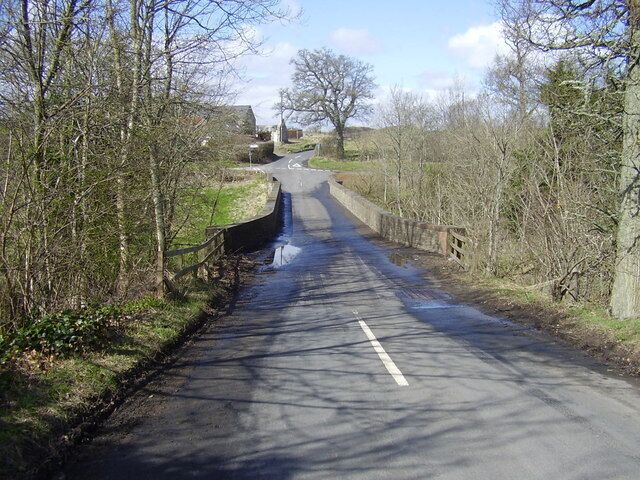 A rural road flanked by trees and a stone wall, leading to a distant building.