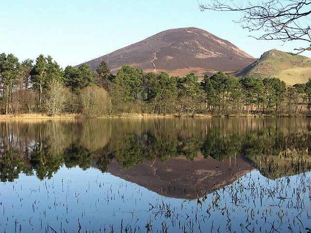 A calm lake with a mountain in the background and trees along the shore.