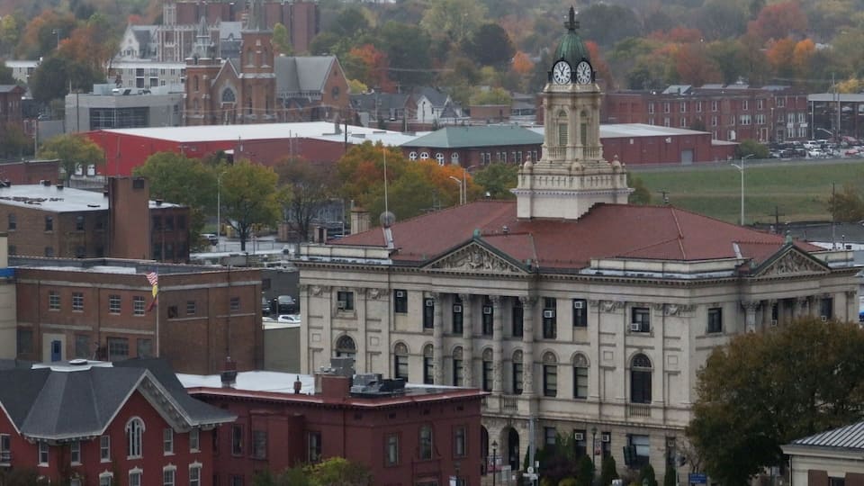 A large building with a clock tower, surrounded by other buildings and trees with autumn foliage.