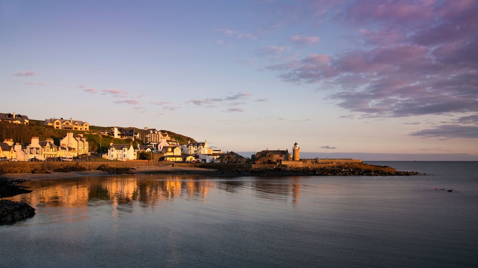 A coastal town with a lighthouse, houses, and a calm sea.