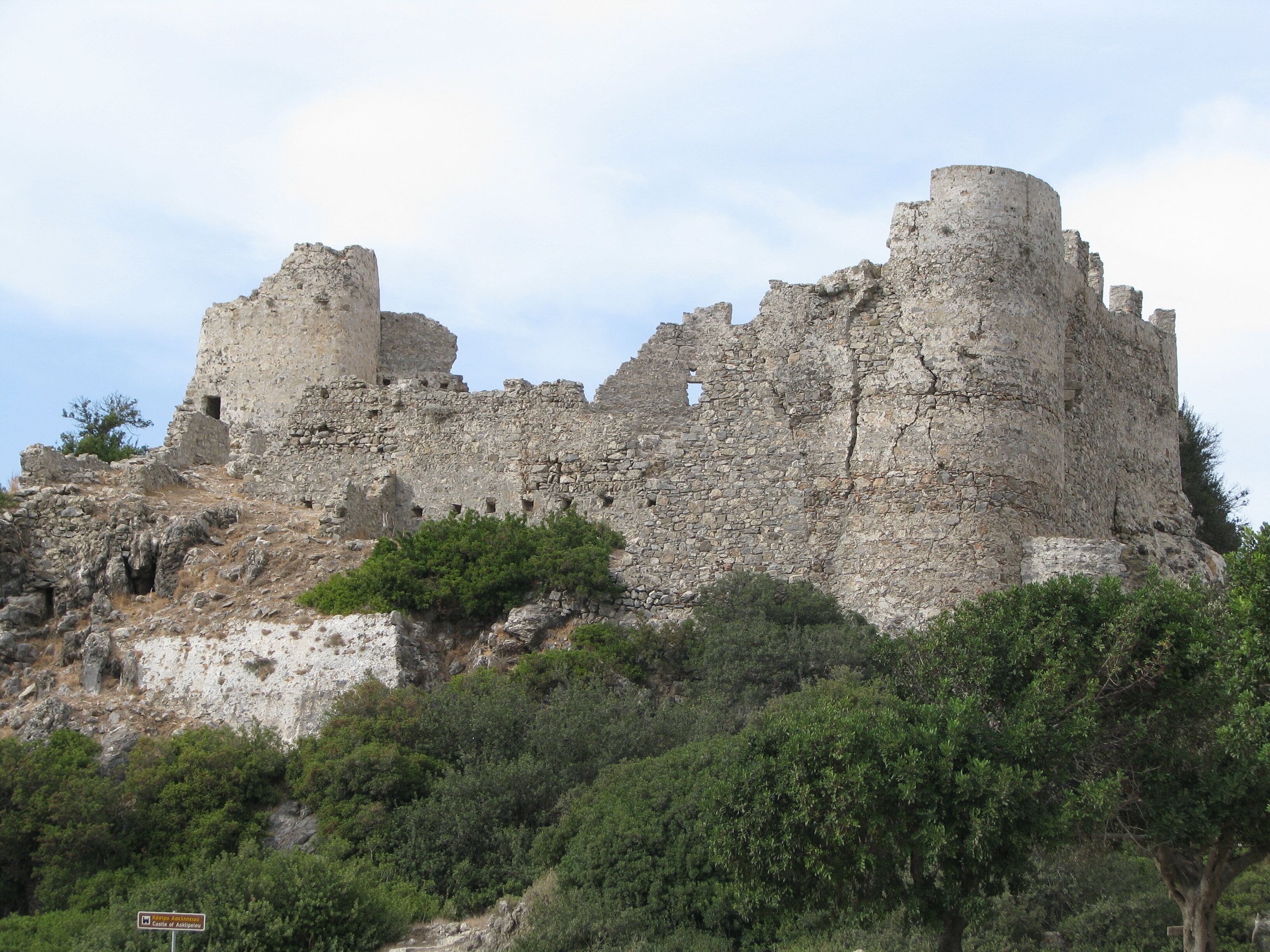 Un castillo de piedra grande y antiguo sobre una colina, rodeado de vegetación.