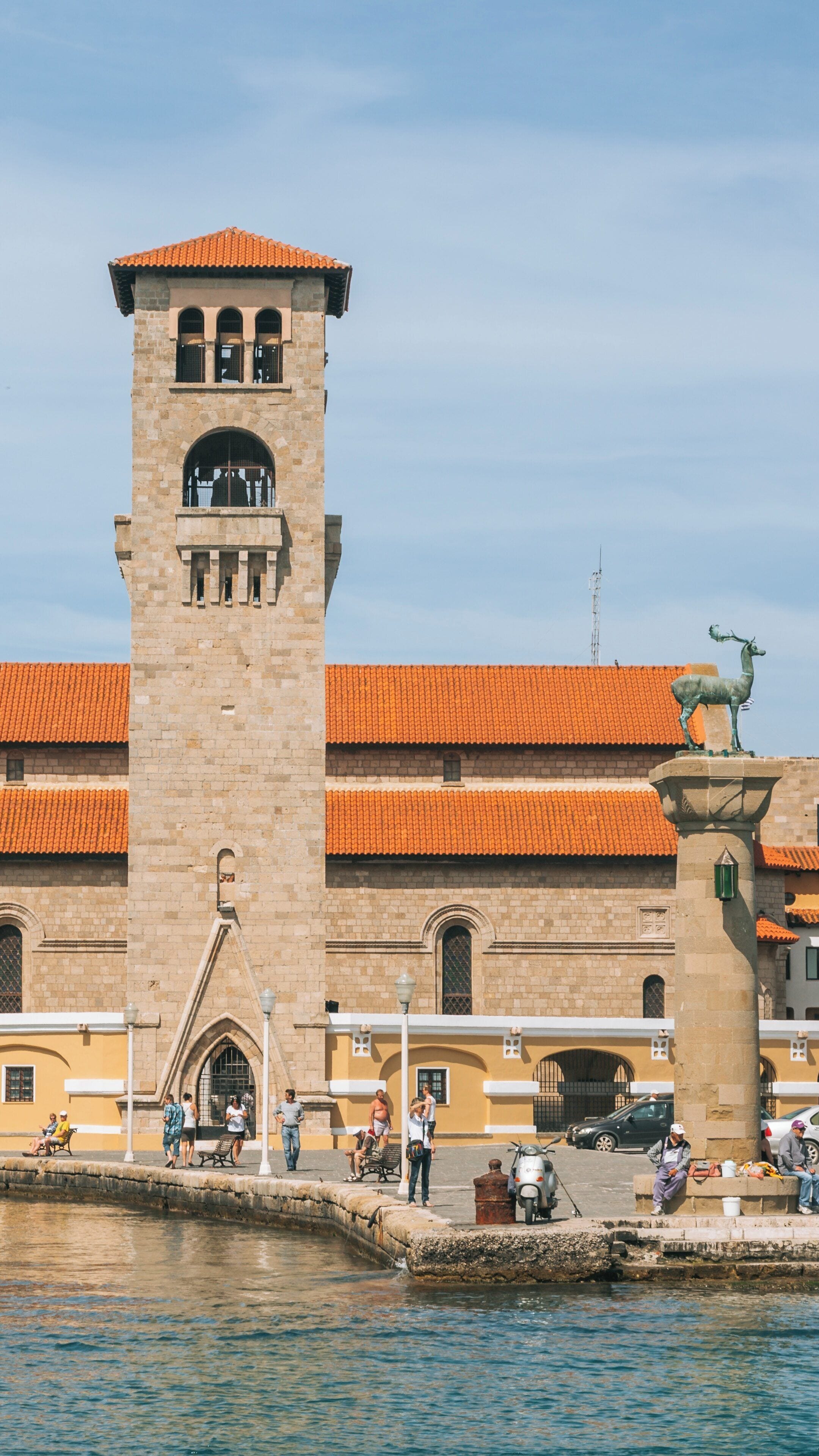 Experience the charm of Rhodes Port with its historic tower and iconic deer statue in South Aegean, Greece under a clear blue sky