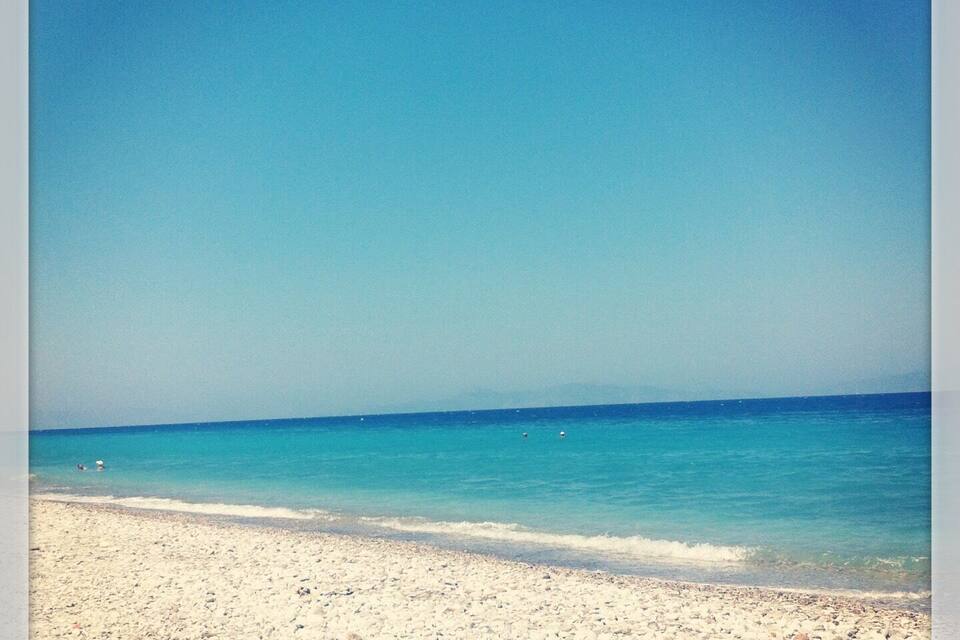 A beach with clear blue water and a sandy shore.