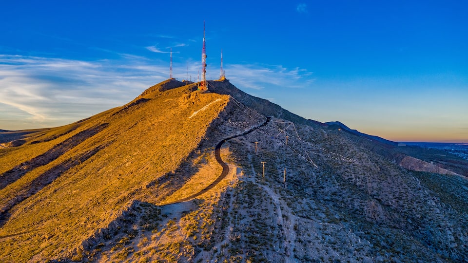 A mountain with a winding road and several communication towers.