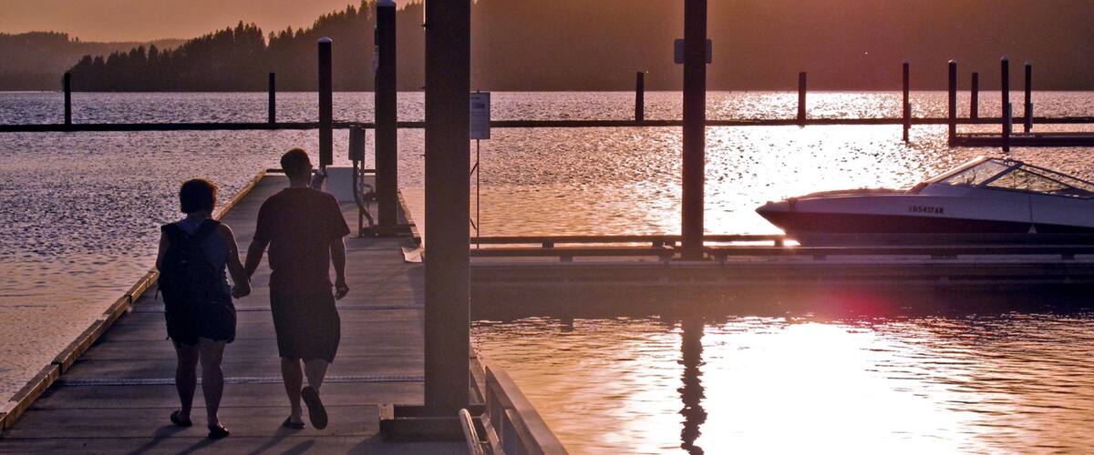 A sunset over a calm lake with a pier, dock, and a boat.